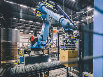 Palletizing warehouse robot handling boxes in an Arvato warehouse for automated logistics and fulfillment operations.