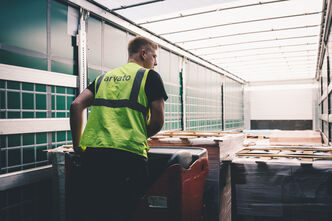 Ein Mitarbeiter mit einer Arvato-Sicherheitsweste transportiert Paletten in einen Lkw