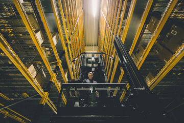 Arvato employee on a narrow aisle forklift in a logistics warehouse with high bay racking