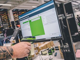 ein Monitor in einem Logistiklager wird mit einem Handscanner gescannt