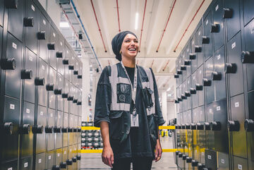 a female arvato warehouse employee smiling between lockers in a warehouse