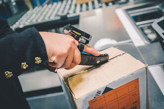 An arvato employee cuts open a returns package with a cutter and finger sensor