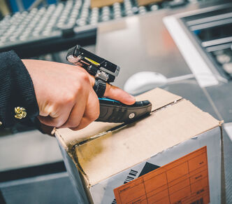 Ein Arvato-Mitarbeiter schneidet ein Retourenpaket mit einem Cutter und Fingersensor auf