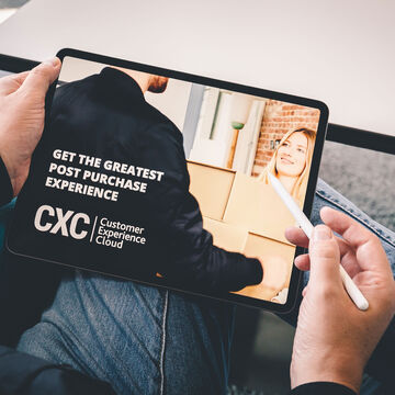 a shoulder view of a person holding a tablet in his lap, the tablet displays Customer Experience Cloud "Get the greatest post purchase experience"