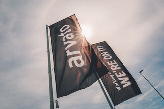 two flags in black one with an arvato logo the otherone displays the lettering, working at arvato we are on it