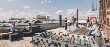 a rooftop terrace under blue skies with a kicker table in the foreground and several employees talking in the background.