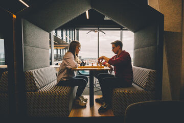 Two employees play chess in front of a large window overlooking the city